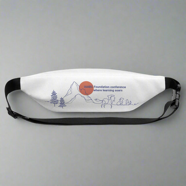 Close up of the back of a white fanny pack with a special visual of mountains, firs, dog, cat and, horse in an outline minimalist style. The drawing highlights the IAABC Foundation conference 2025 in Colorado Springs and the Garden of Gods. Written: " IAABC Foundation conference where learning soars"